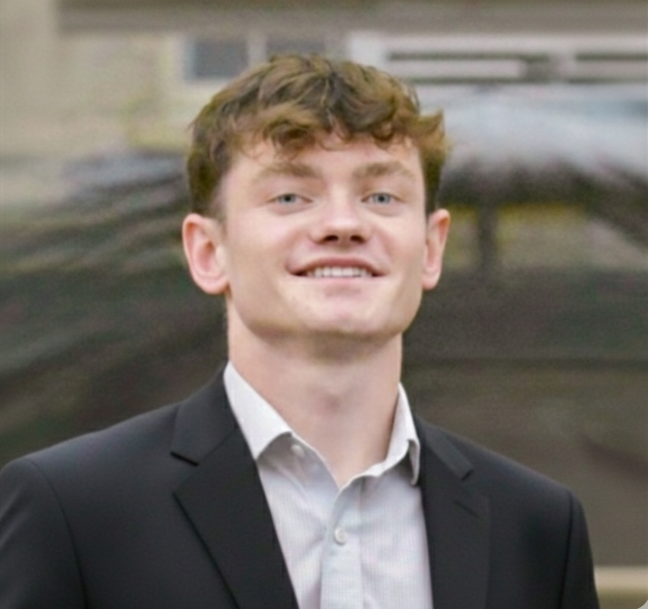Jacob Berko wearing a dark suit jacket and white shirt against a softly blurred background