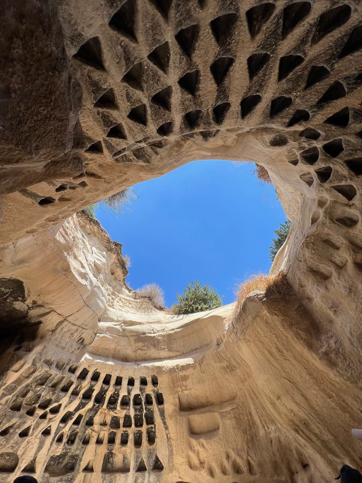 Carved sandstone chamber with rows of wall niches surrounding an opening to blue sky