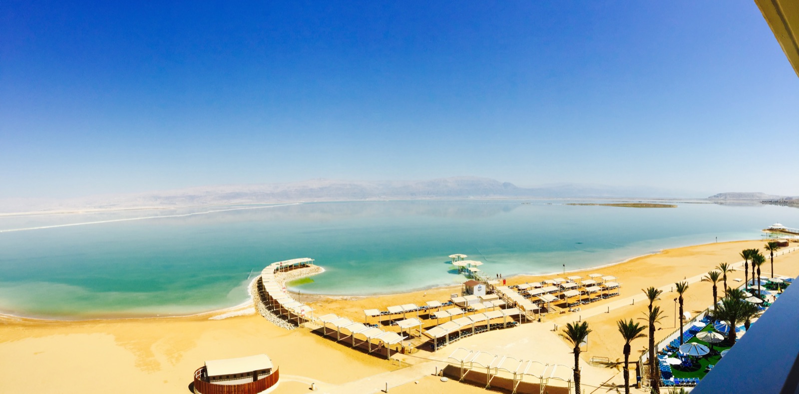 Turquoise water, sandy resort beach, white sun shelters, and hazy desert mountains