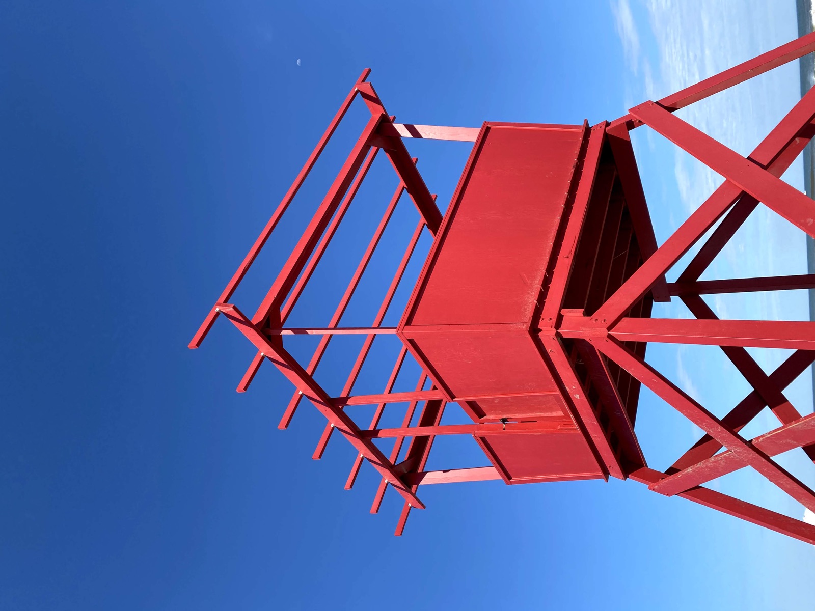Red wooden lifeguard tower against a deep blue sky with a pale moon