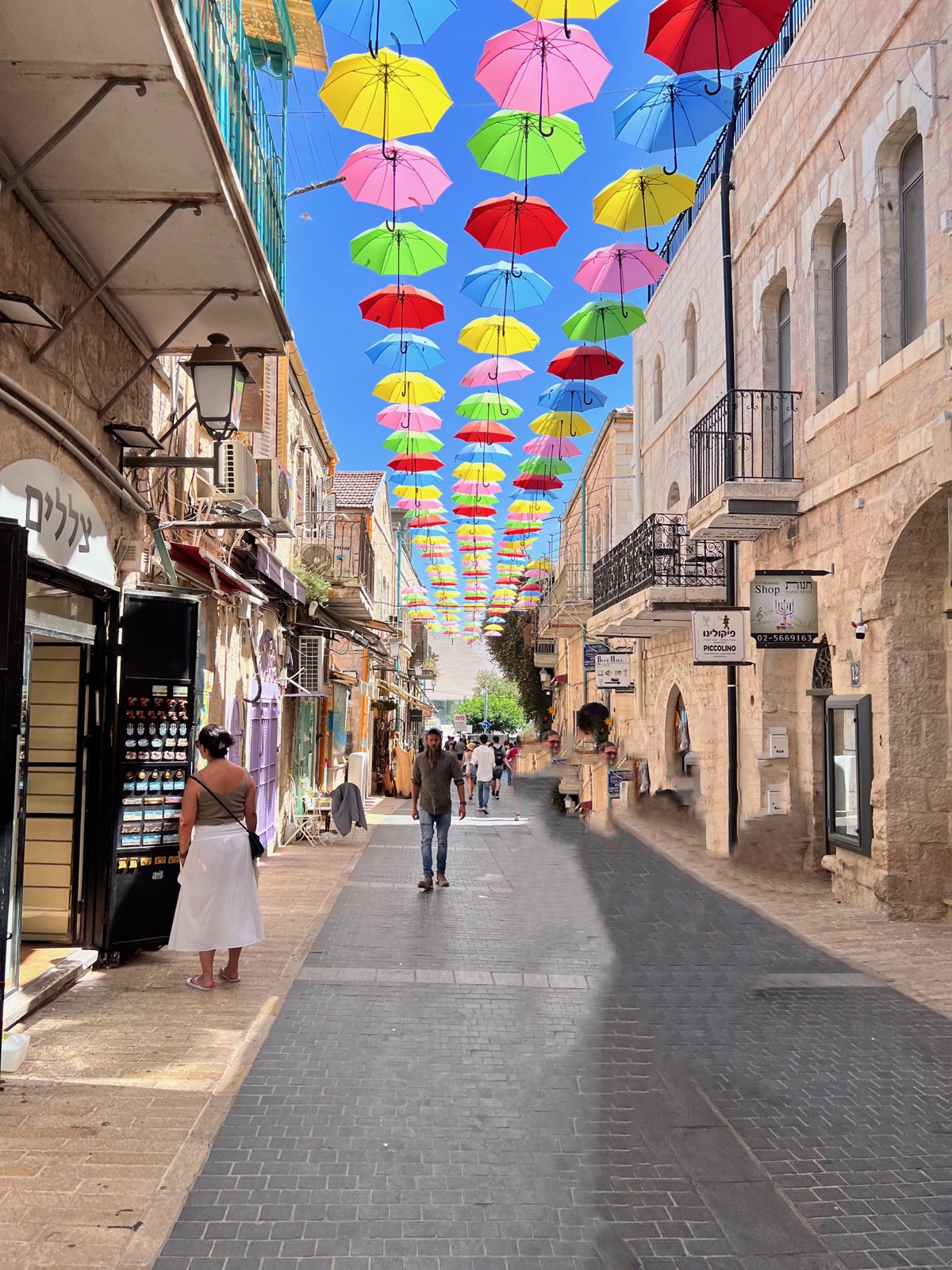 Colorful umbrellas suspended above pedestrians on a narrow stone-lined shopping street