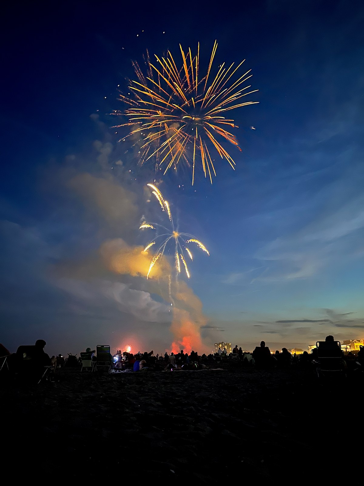 Golden fireworks bursting above a seated beach crowd at dusk