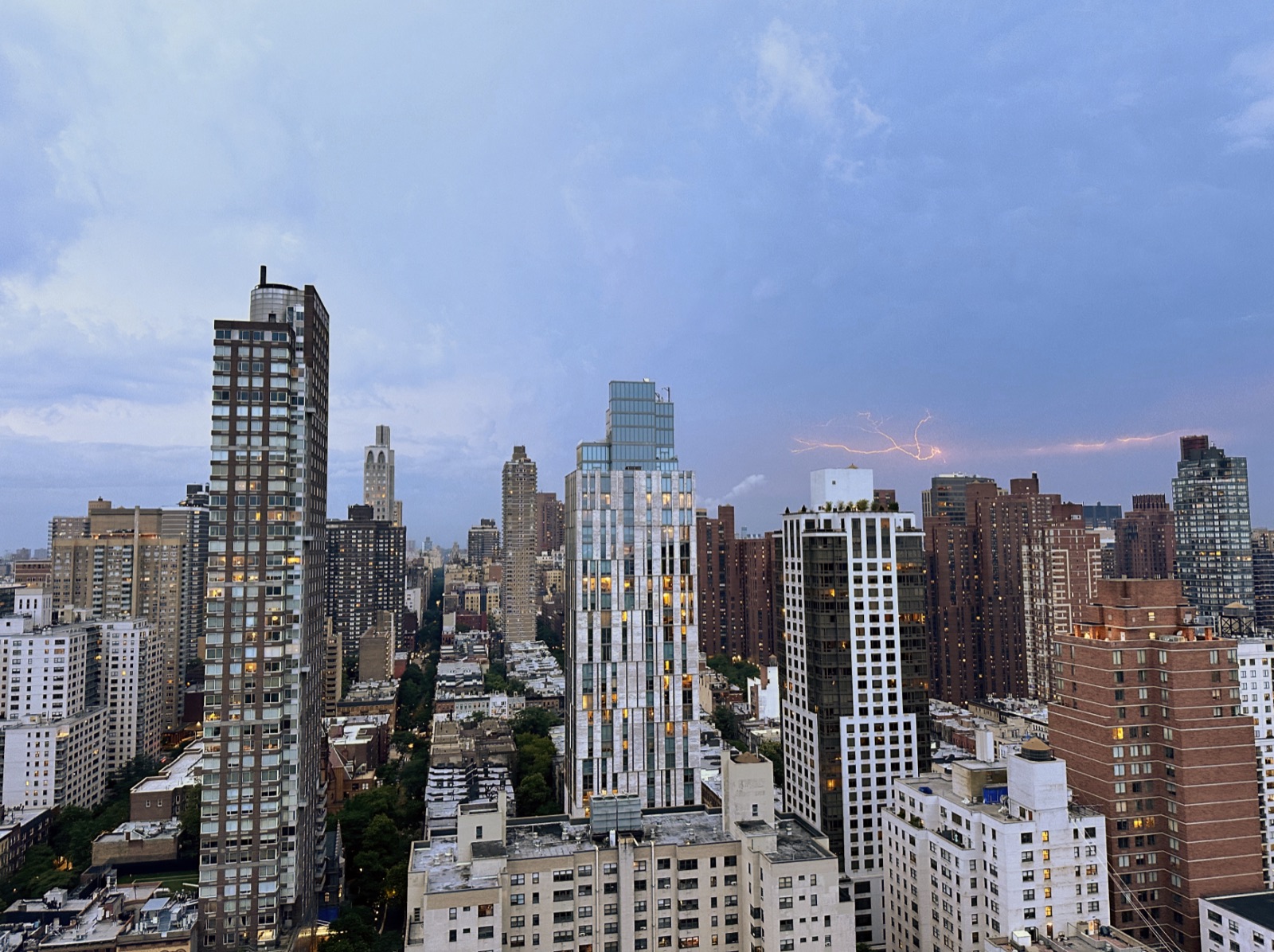 Branching lightning stretching across storm clouds behind a dense city skyline at dusk