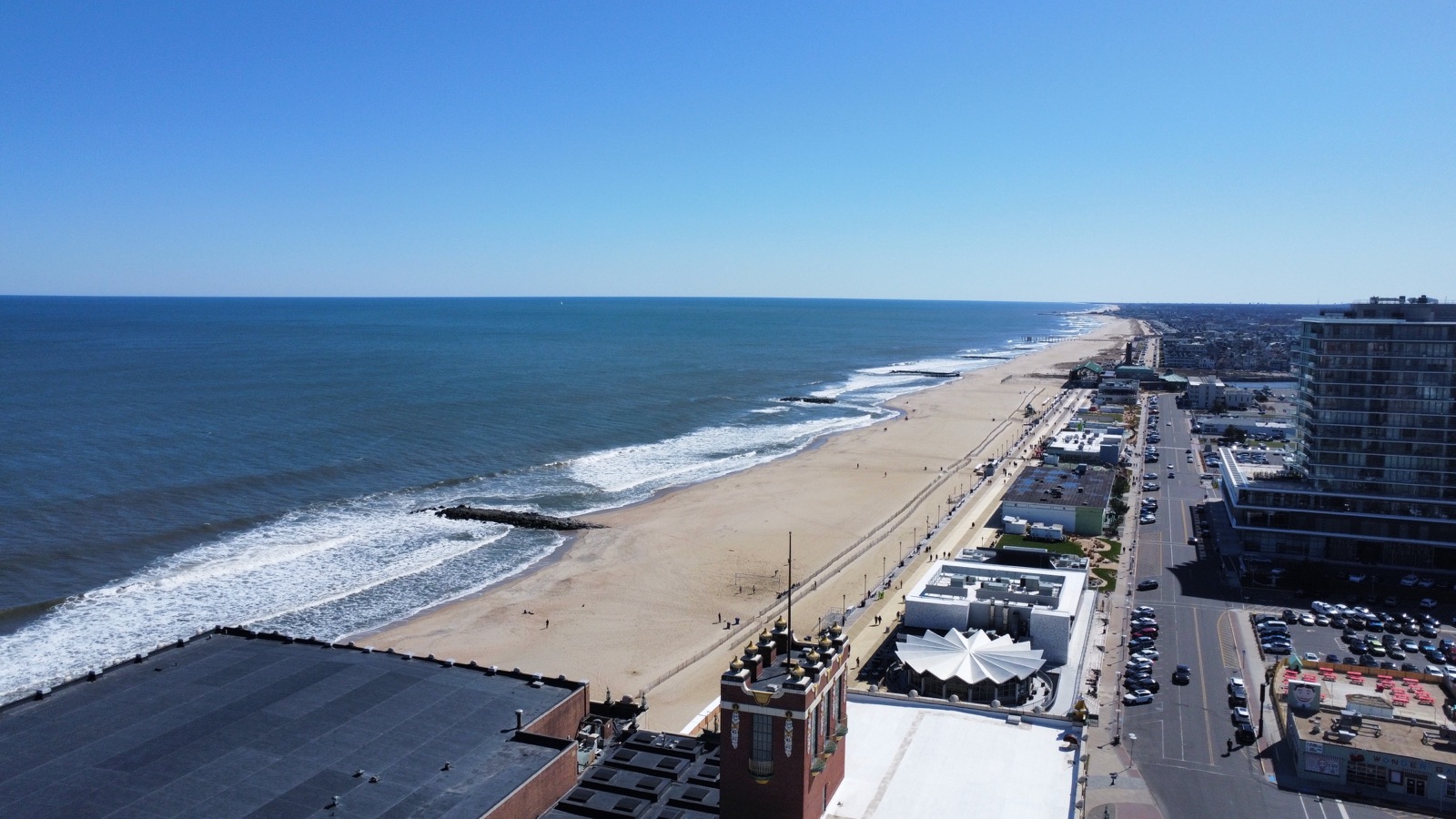 Aerial panorama of a sandy beach, ocean waves, jetties, and beachfront buildings
