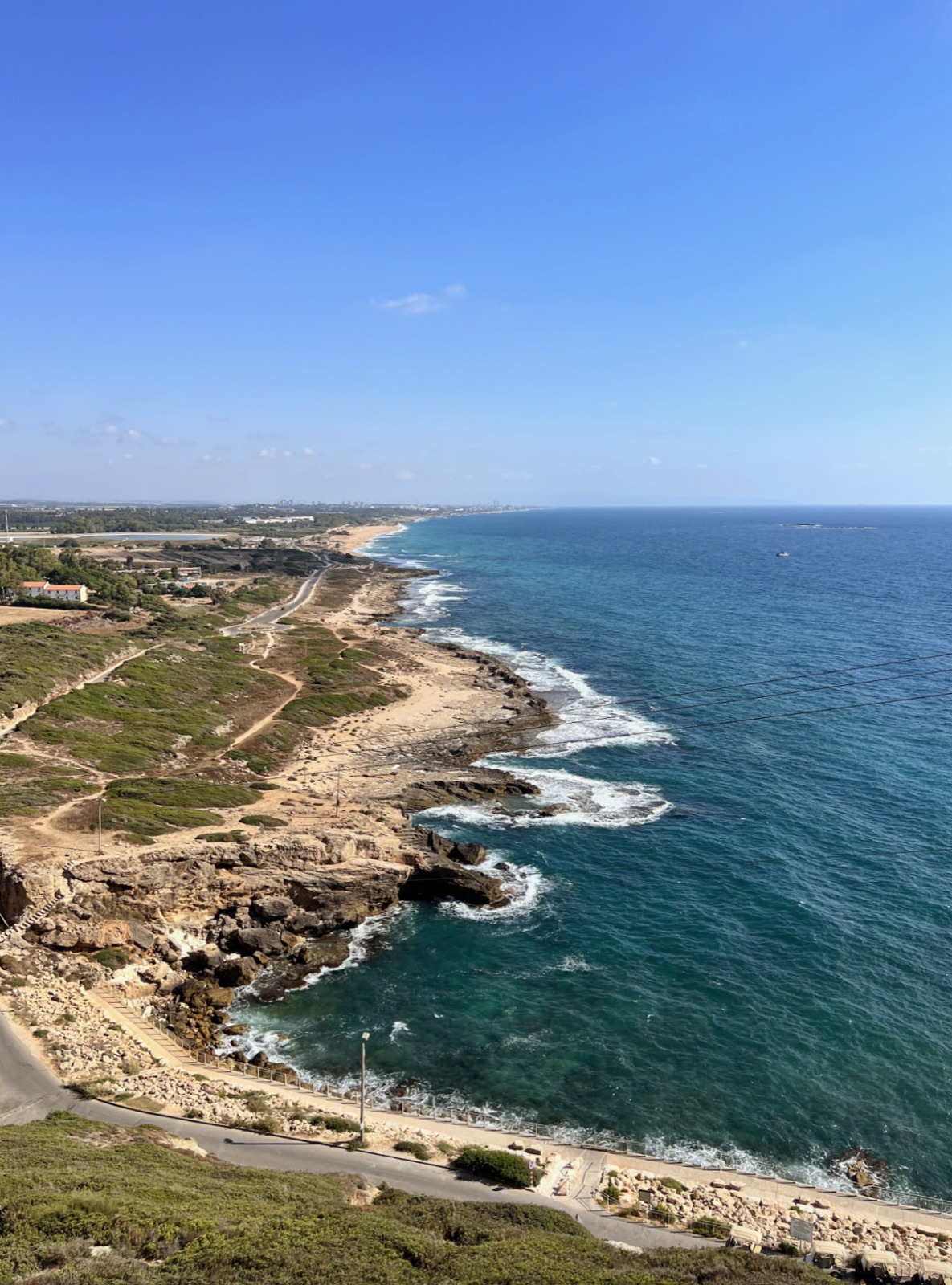 Elevated view along a rocky coastline with turquoise water, coastal roads, and footpaths