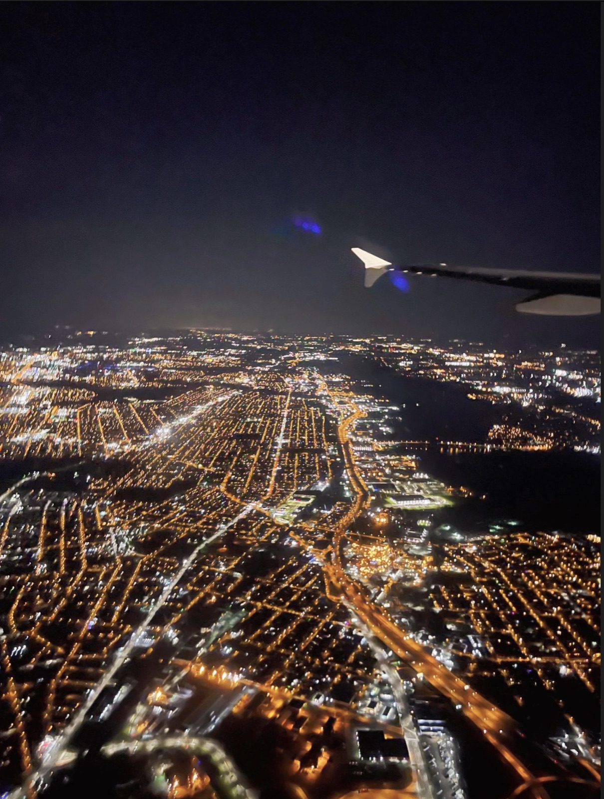 Illuminated city streets and waterways at night beneath an airplane wing