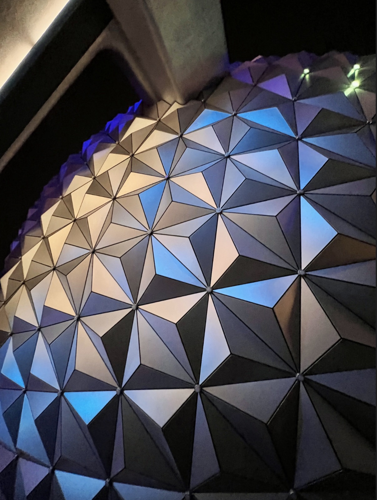 Faceted triangular wall panels illuminated blue, purple, and warm white at night
