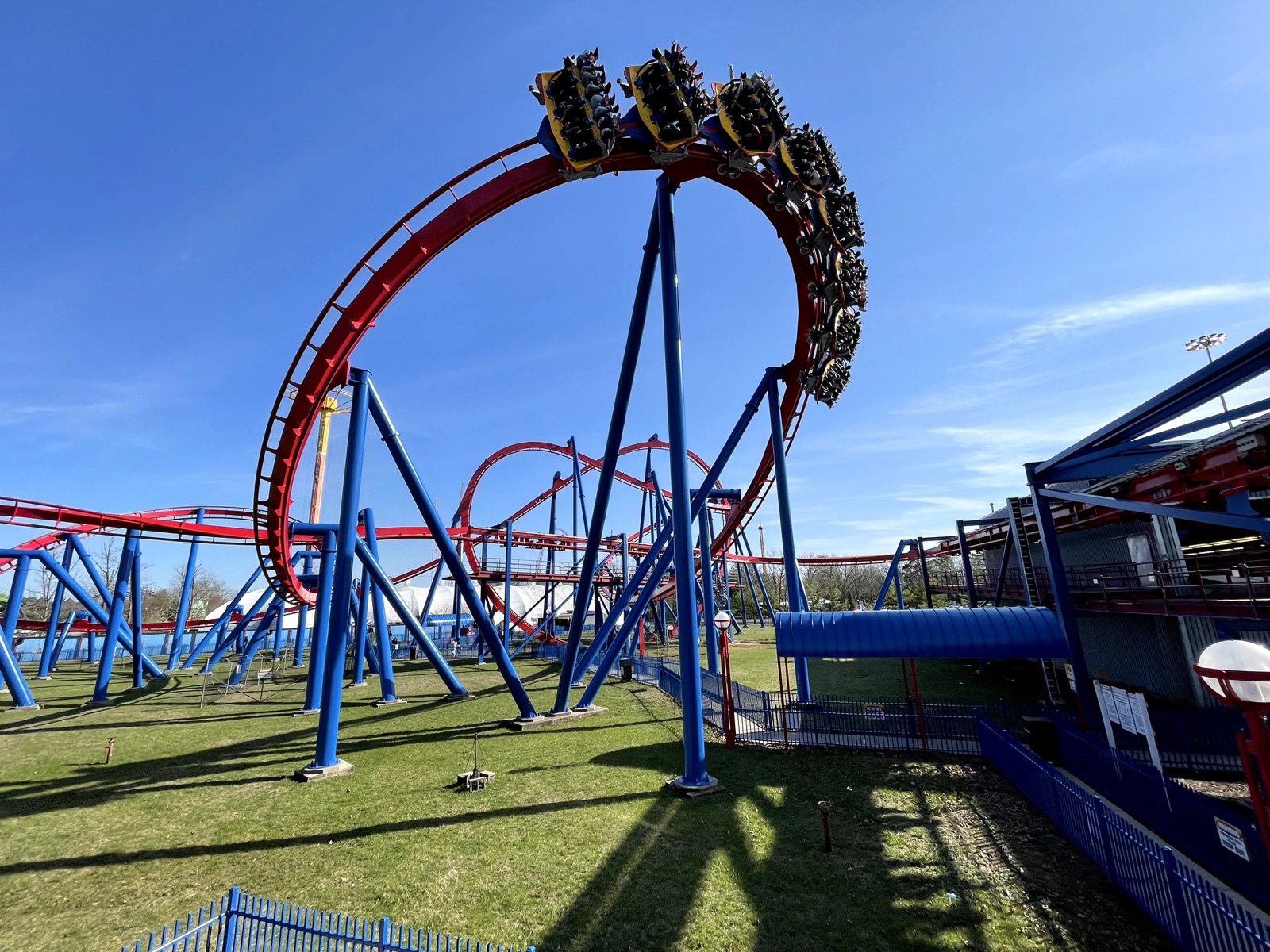Inverted roller coaster train crossing a red loop supported by blue columns